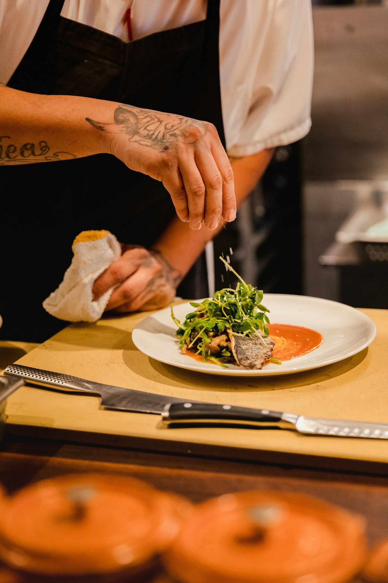 Chef plating a dish garnished with fresh microgreens in a restaurant kitchen