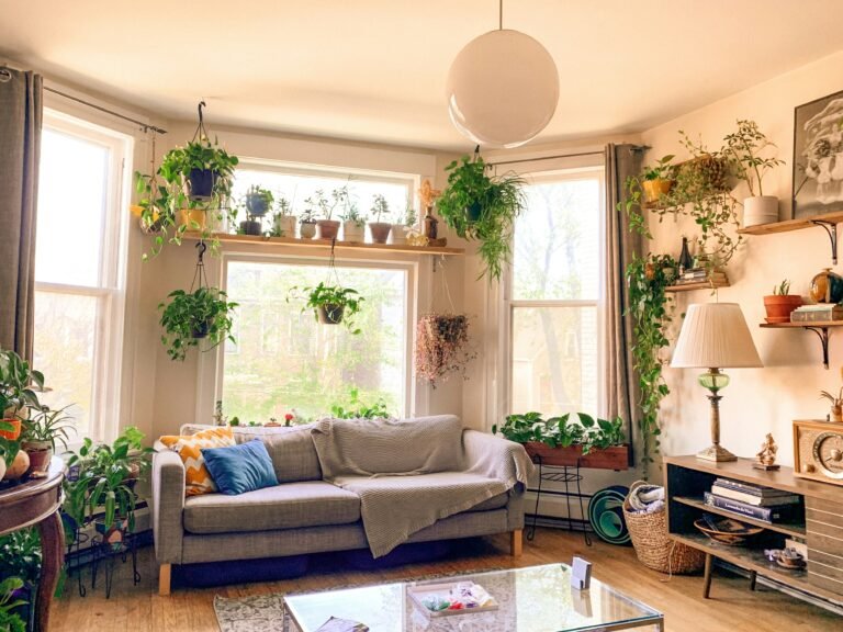 A cozy plant corner in a small apartment with a wooden plant stand, layered houseplants, and warm natural light